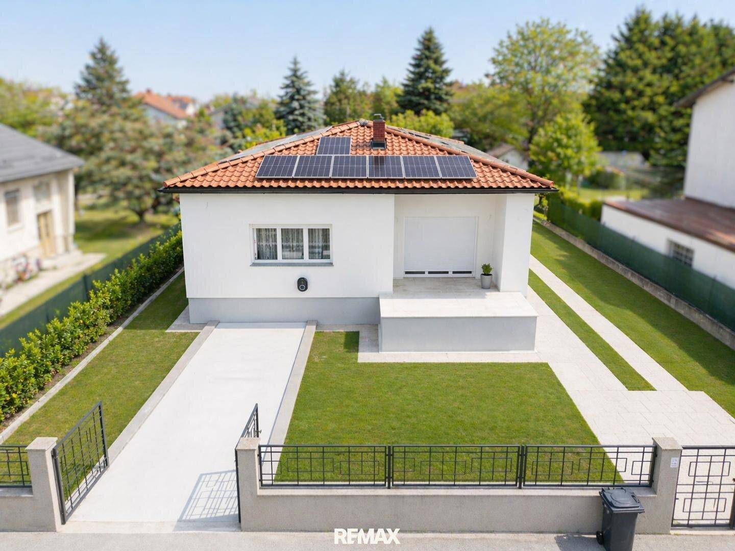 Modernes Einfamilienhaus mit weißer Fassade, rotem Ziegeldach und Solaranlage auf dem Dach.