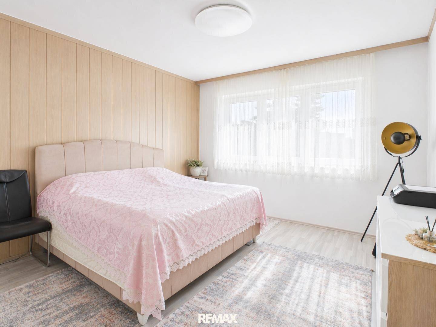 Gemütliches Schlafzimmer mit Doppelbett, Holzwandverkleidung und viel Tageslicht.