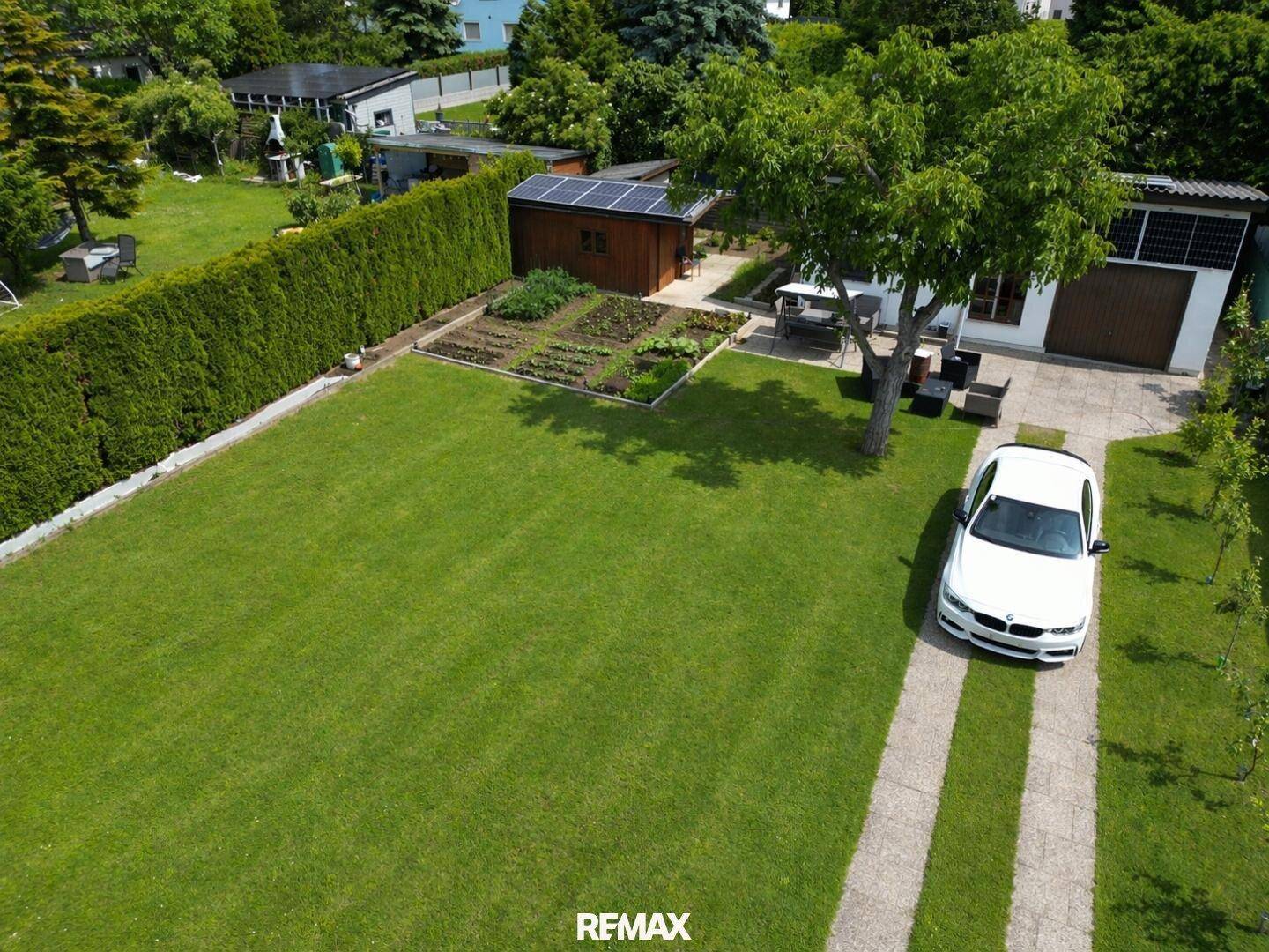 Großer grüner Garten mit Rasenfläche, Gartenhaus, Gemüsebeet und schattenspendenden Bäumen.