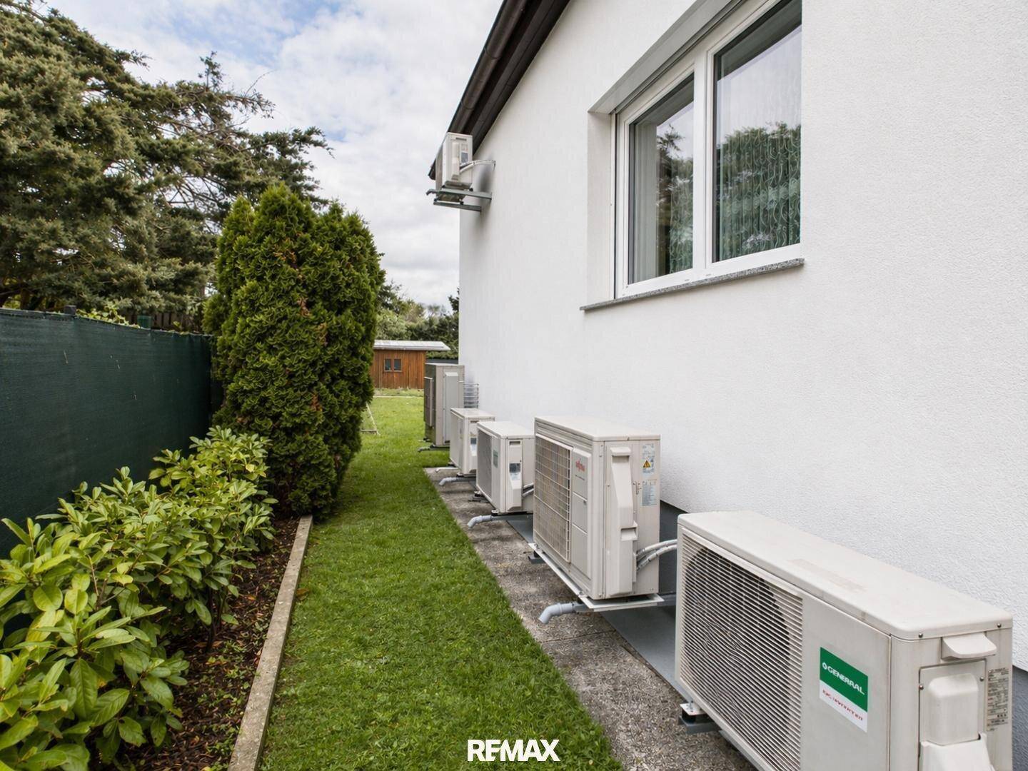 Mehrere Klimaanlagen-Außengeräte an der Hauswand mit Blick auf den Garten.