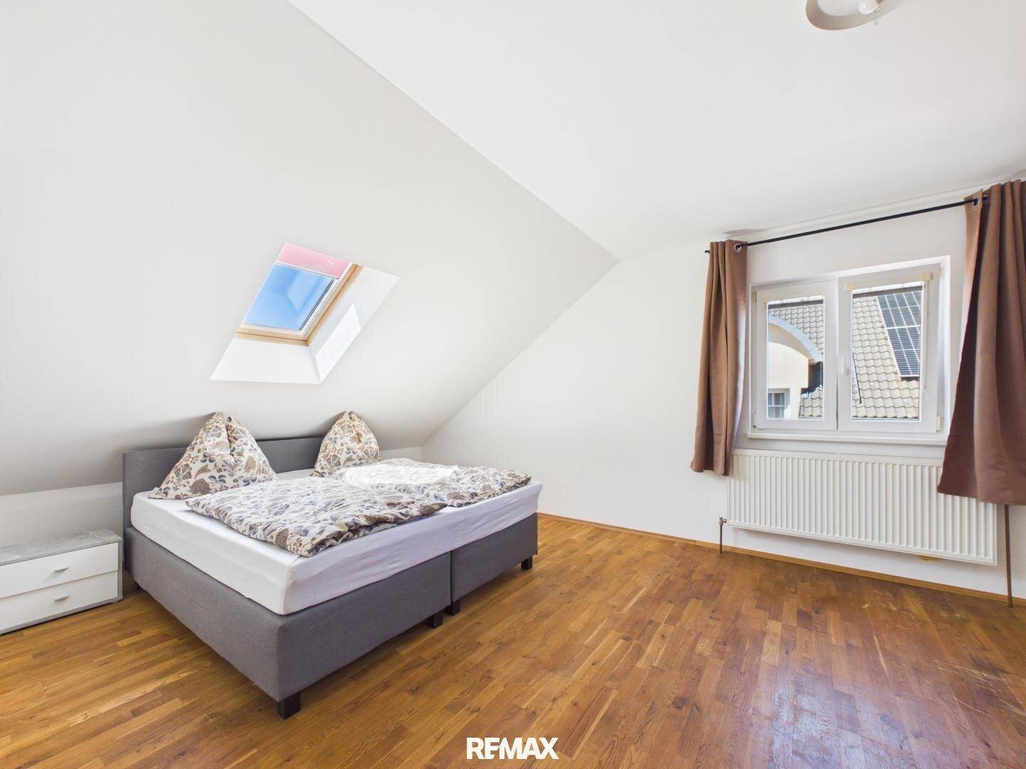 Helles Schlafzimmer im Dachgeschoss mit Holzboden, Doppelbett und Dachfenster.