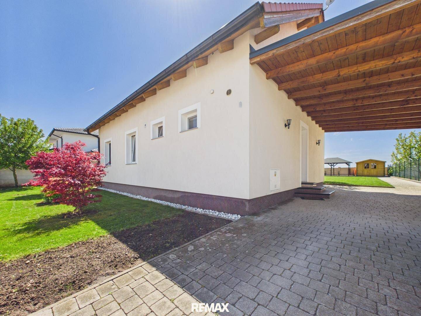 Seitenansicht des Hauses mit gepflasterter Einfahrt und einem überdachten Stellplatz.