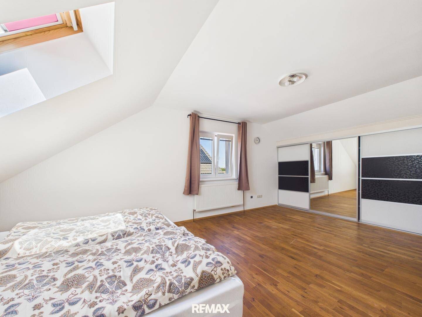 Geräumiges Schlafzimmer im Dachgeschoss mit Holzboden und großen Spiegelschränken.