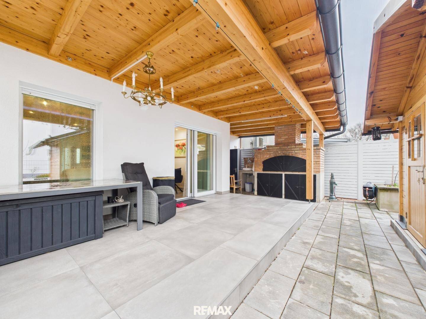 Überdachte Terrasse mit Holzdach, Sitzgelegenheiten und integriertem Grillbereich.