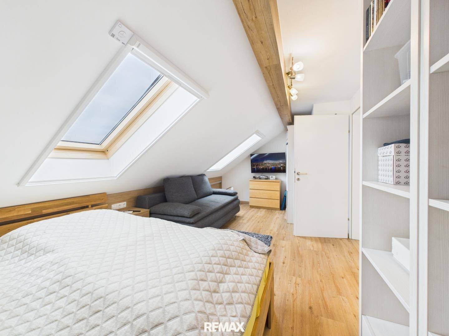 Schlafzimmer im Dachgeschoss mit schrägen Wänden, zwei Dachfenstern und Holzboden.