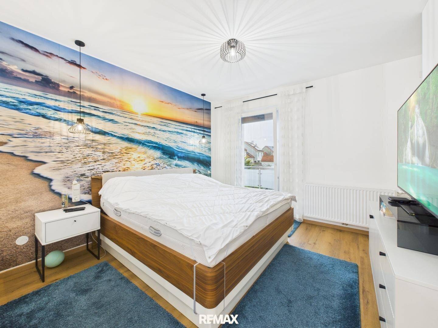 Schlafzimmer mit beeindruckender Strandtapete, Doppelbett und Zugang zum Balkon.