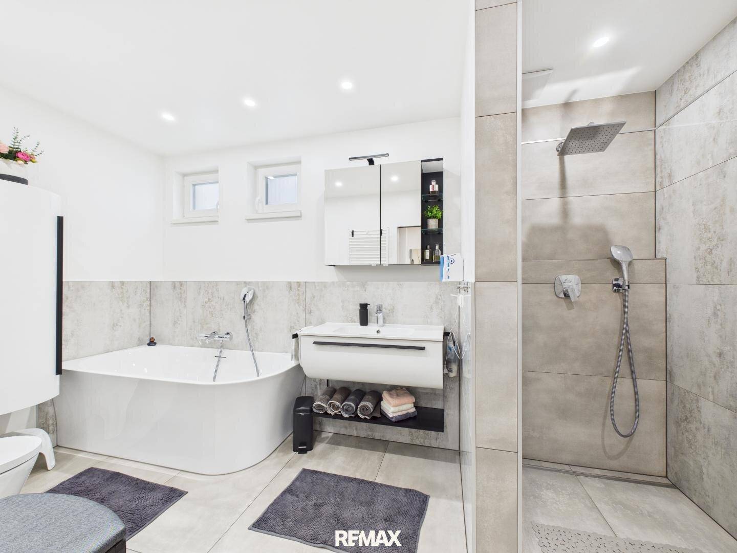 Modernes Badezimmer mit Badewanne, ebenerdiger Dusche und Fenster für Tageslicht.