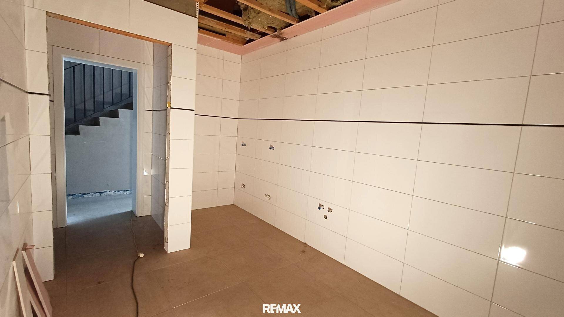 Raum im Rohbau mit weißen Wandfliesen und sichtbaren Installationen für ein Badezimmer.