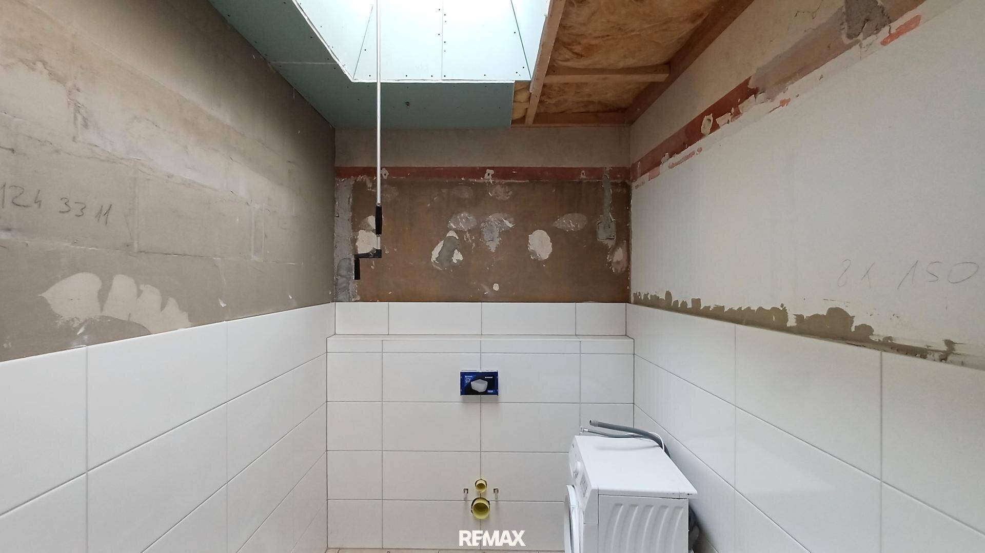 Kleiner Raum im Rohbau mit Wandfliesen, vorbereitet für ein WC und eine Waschmaschine.