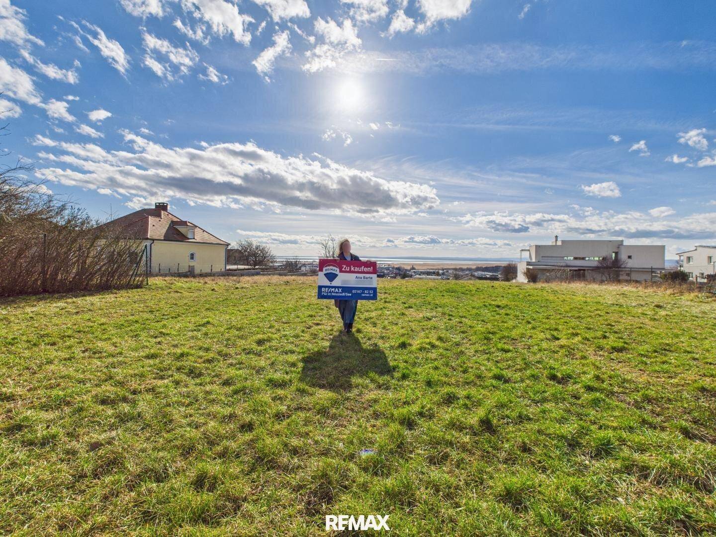 Helles Grundstück mit weitem Blick über die Landschaft bis zum See, präsentiert mit Verkaufsschild.