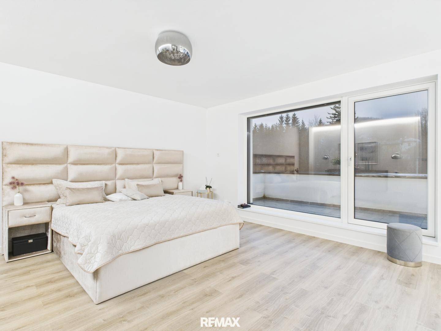 Elegantes Schlafzimmer mit großem Bett, hellem Holzboden und bodentiefen Fenstern.