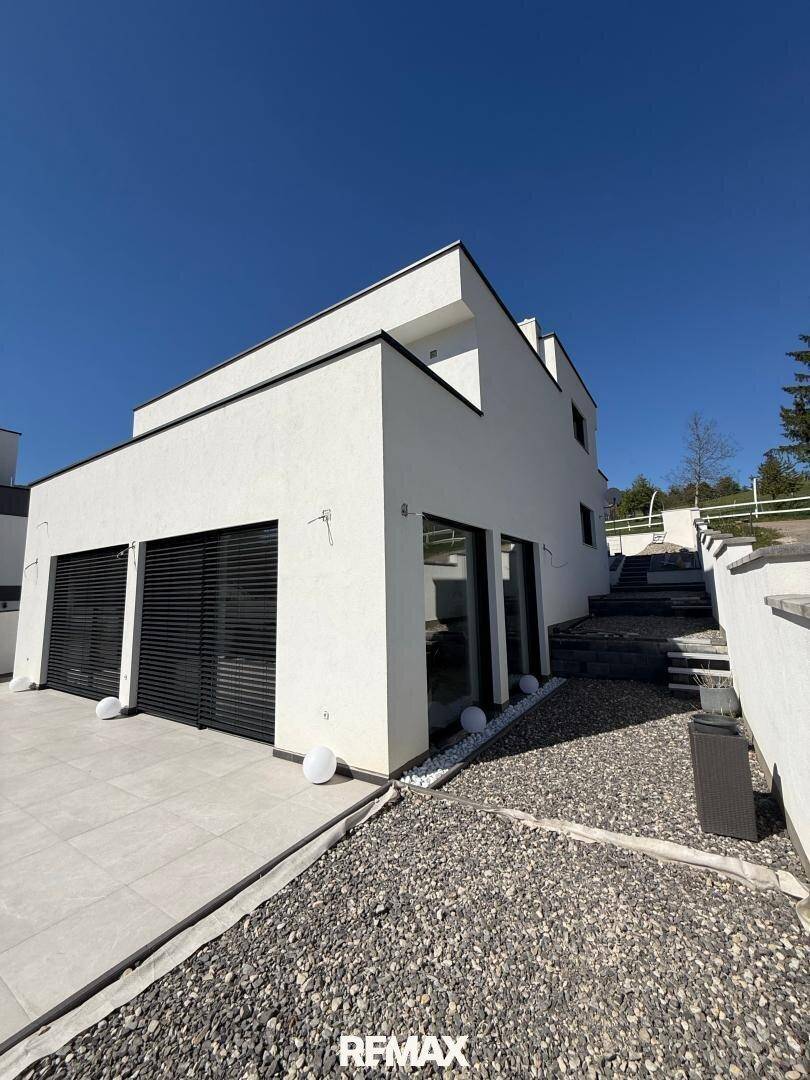 Seitliche Ansicht der modernen Villa mit Garagentoren und gepflastertem Zugangsbereich.