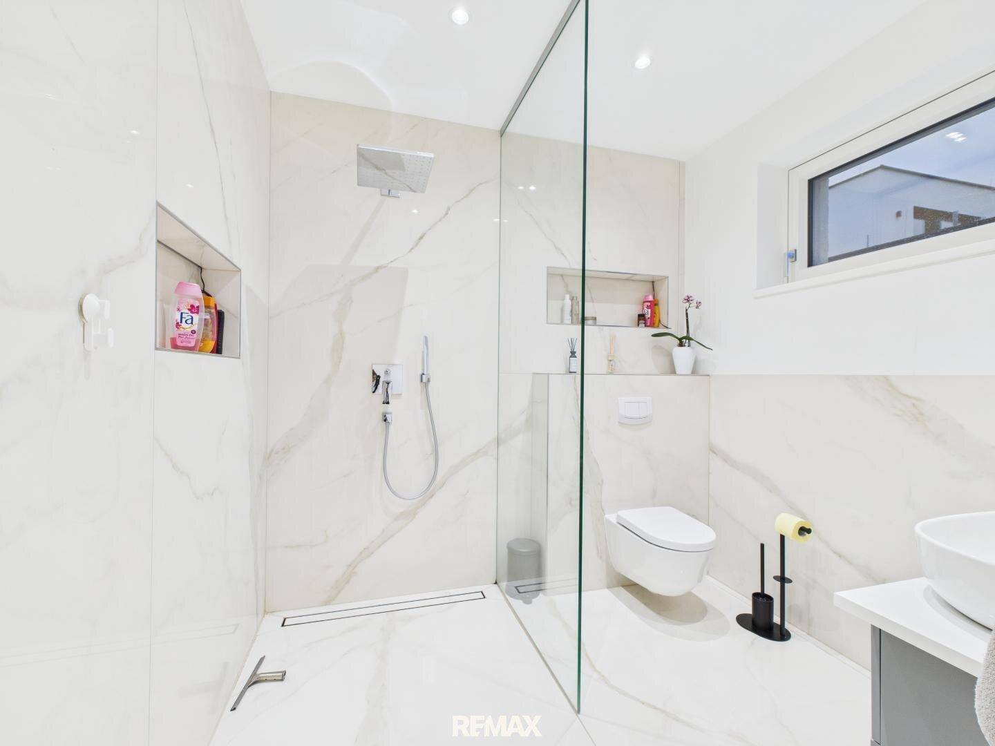 Elegantes Badezimmer mit großer begehbarer Dusche, Marmorfliesen und Fenster.