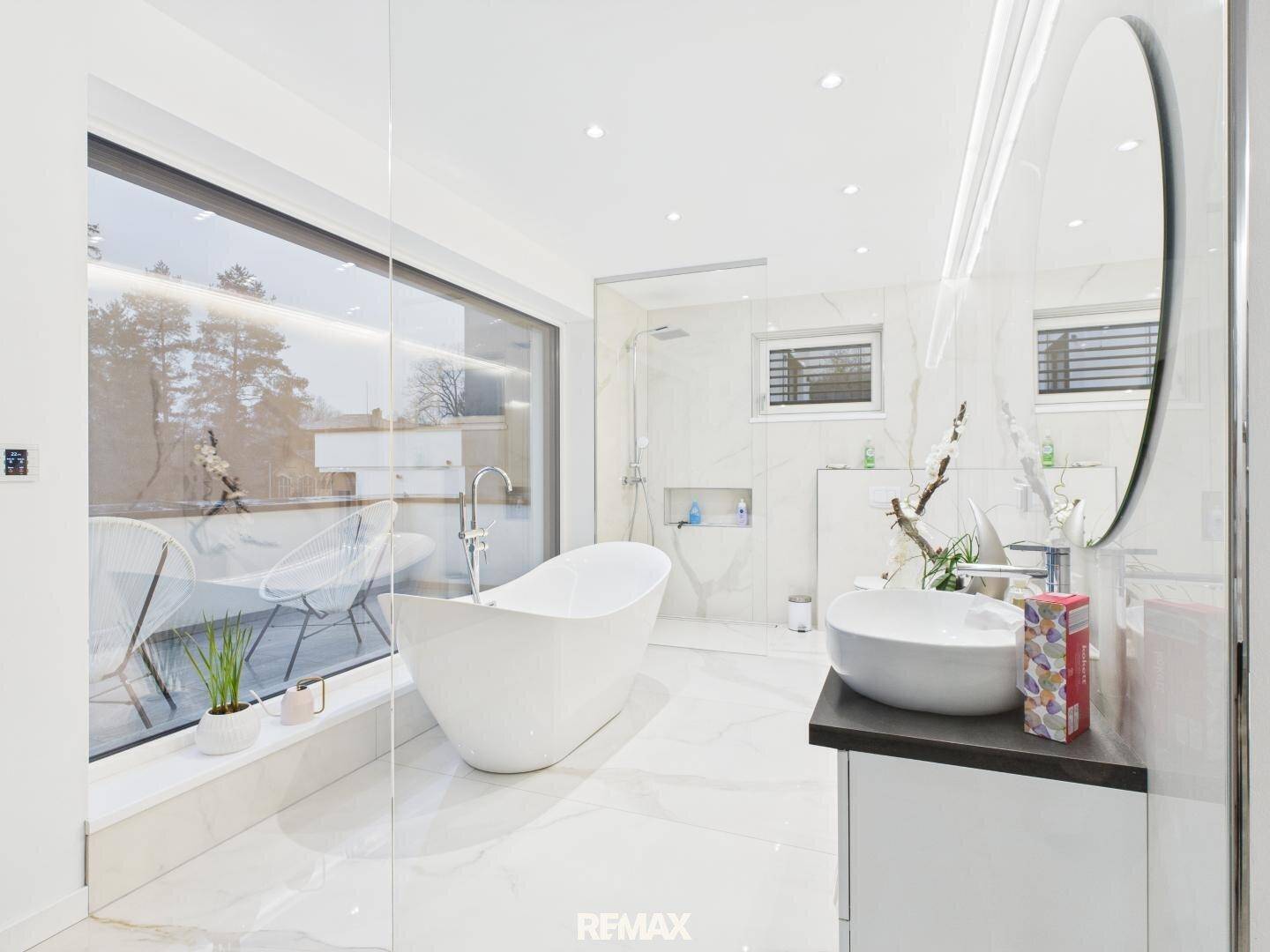 Modernes Badezimmer mit freistehender Badewanne, großem Fenster und eleganten Marmoroberflächen.