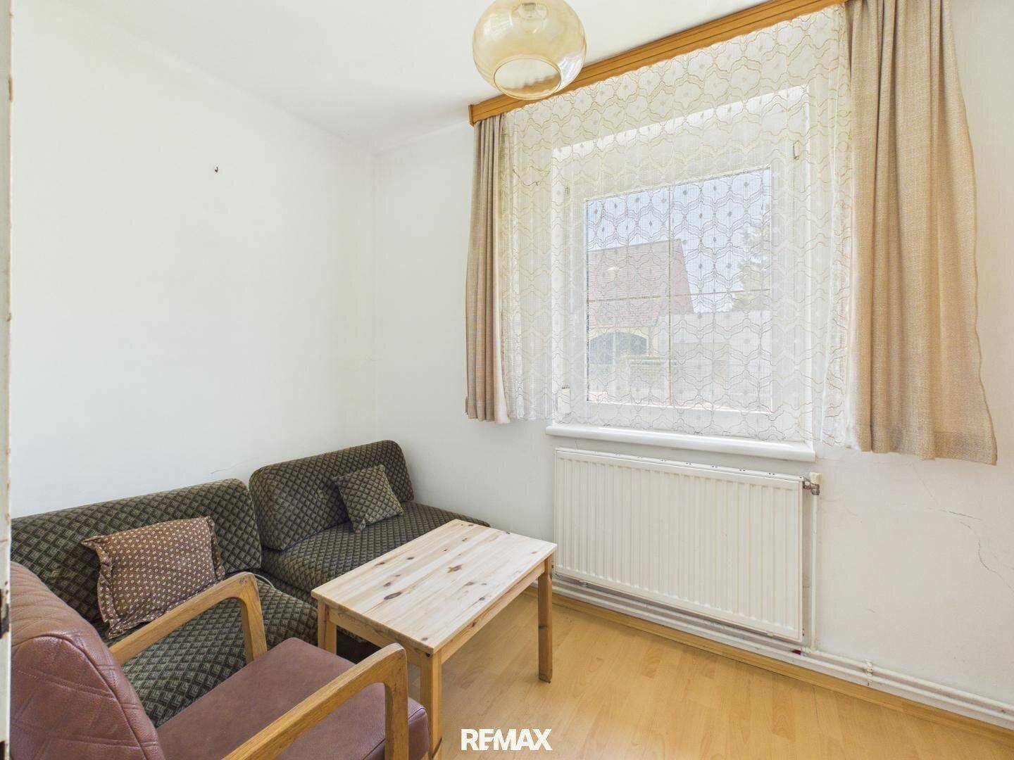 Kleiner Wohnbereich mit Sofa, Holztisch und Fenster mit Heizkörper.