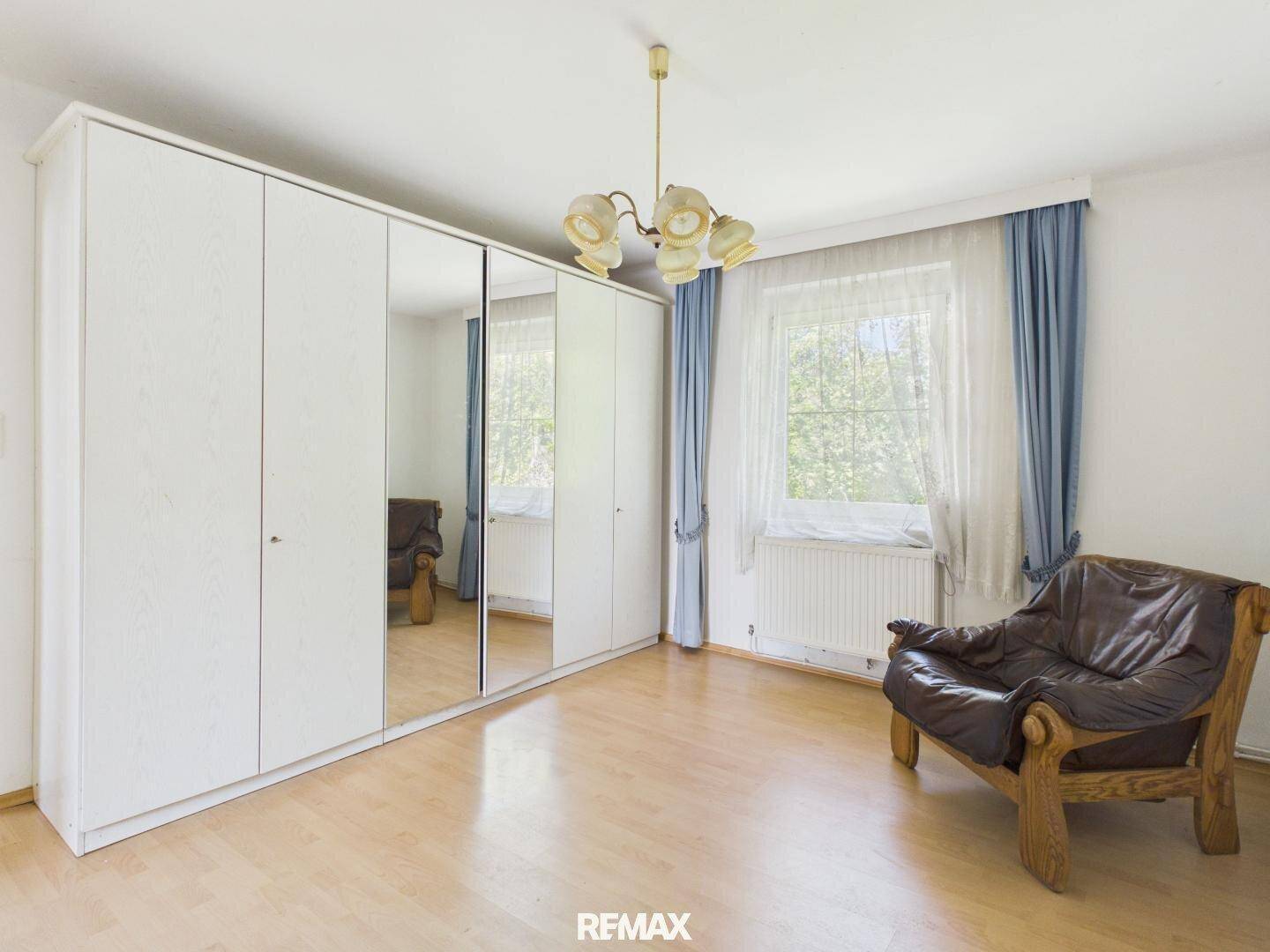 Schlafzimmer mit großem weißen Kleiderschrank, Spiegeltüren und einem bequemen Sessel.