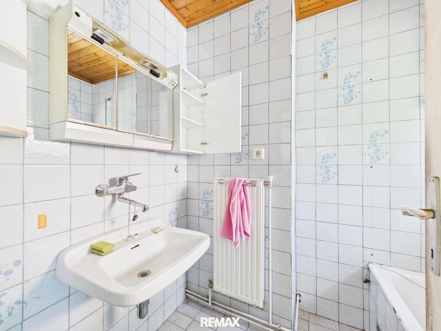 Badezimmer mit hellblauen Fliesen, Waschbecken, Spiegelschrank und Holzdecke.