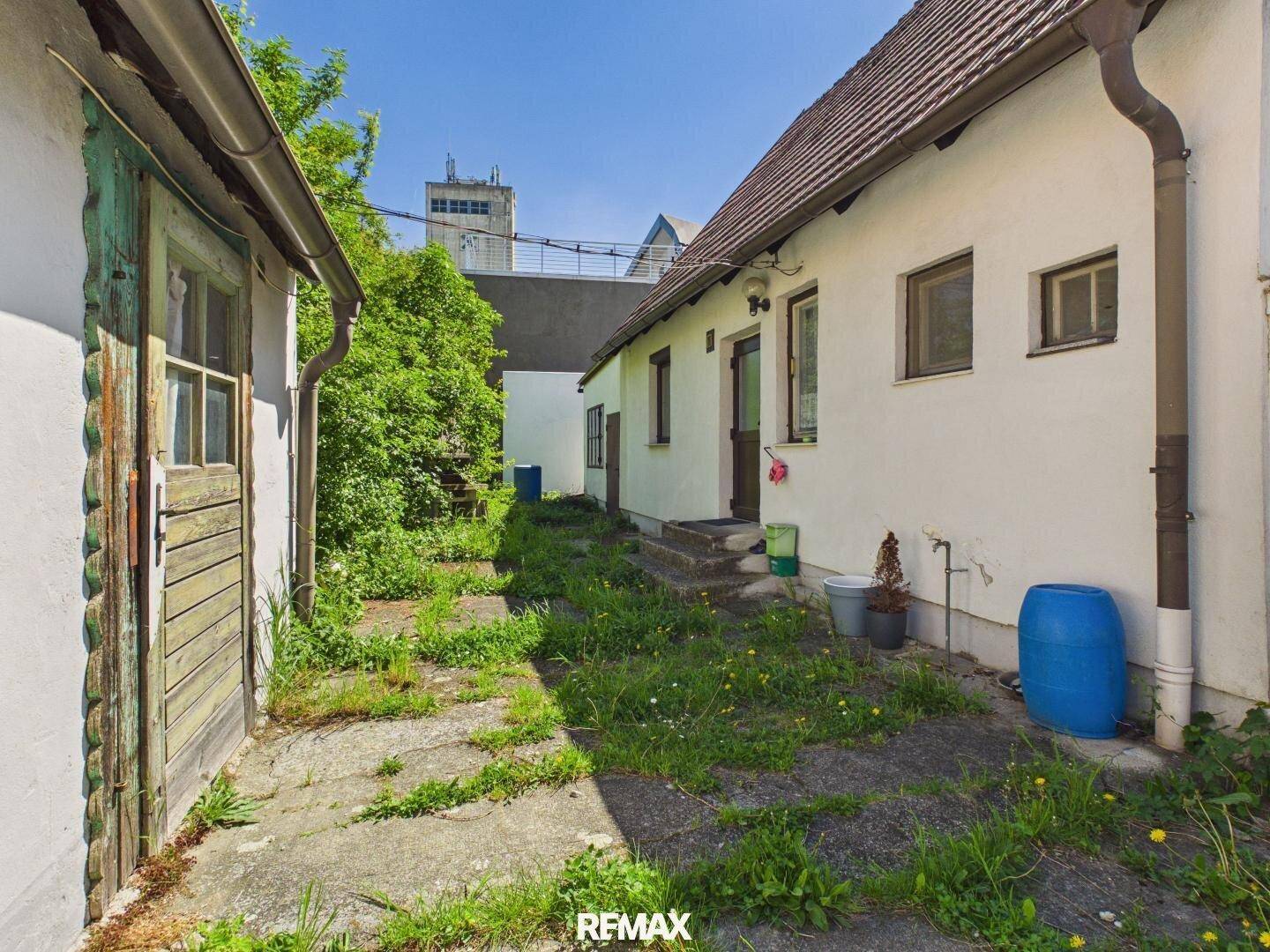 Seitenansicht des Hauses mit einem schmalen, zugewachsenen Weg und einem Nebengebäude.