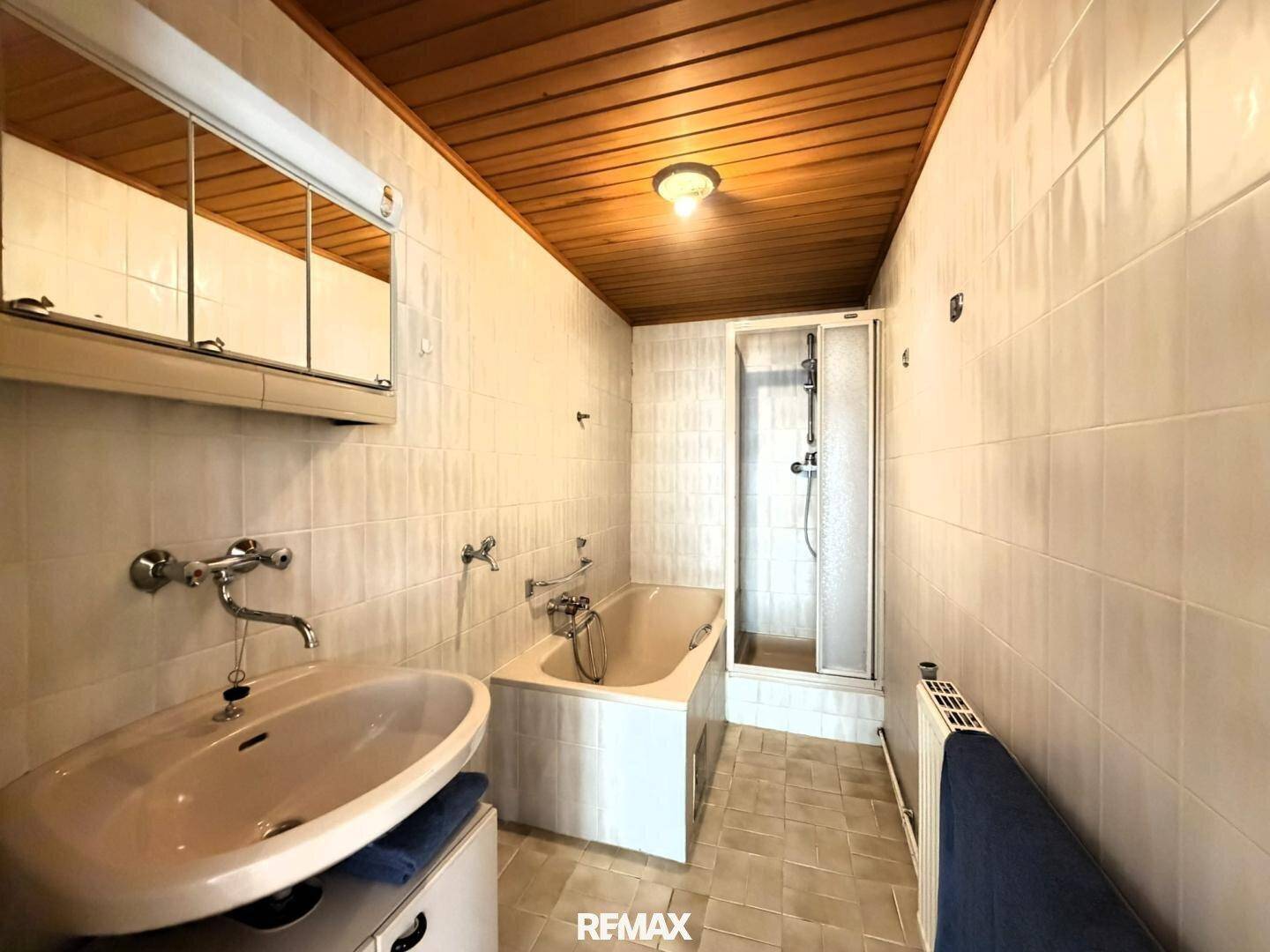 Badezimmer mit Holzdecke, Badewanne und separater Dusche, in hellem Fliesen-Design.