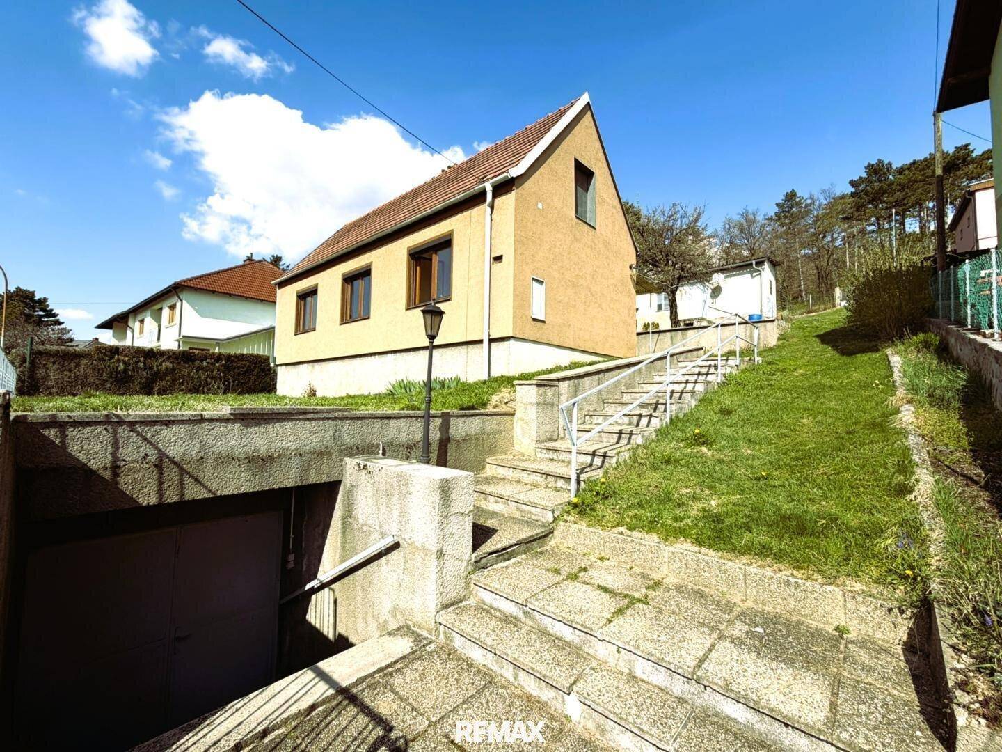 Zugang zum Haus mit Außentreppe und Einfahrt zur Tiefgarage, umgeben von Grünflächen.