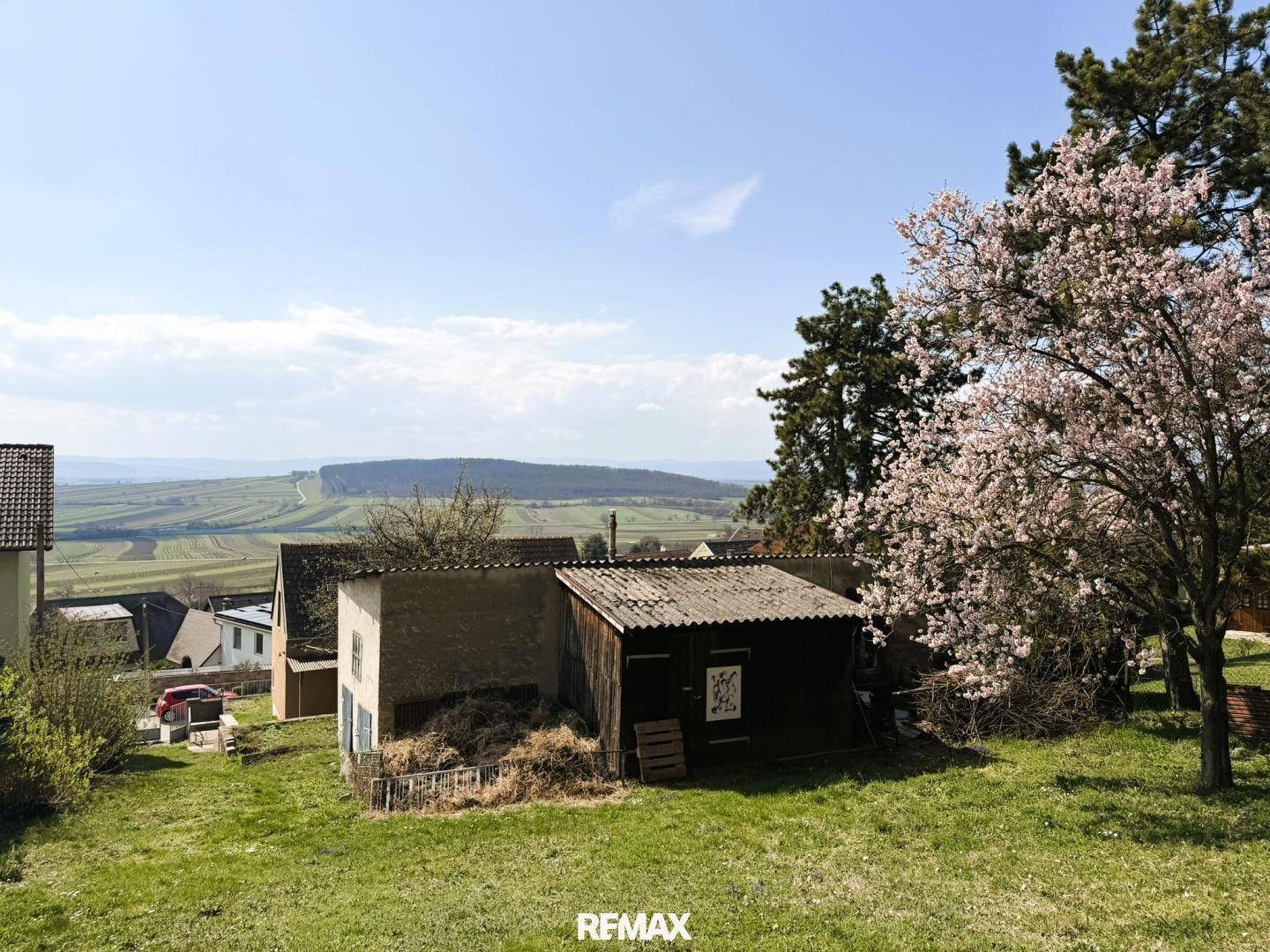 Gartenbereich mit Schuppen und blühendem Baum, bietet weite Aussicht auf die Landschaft.