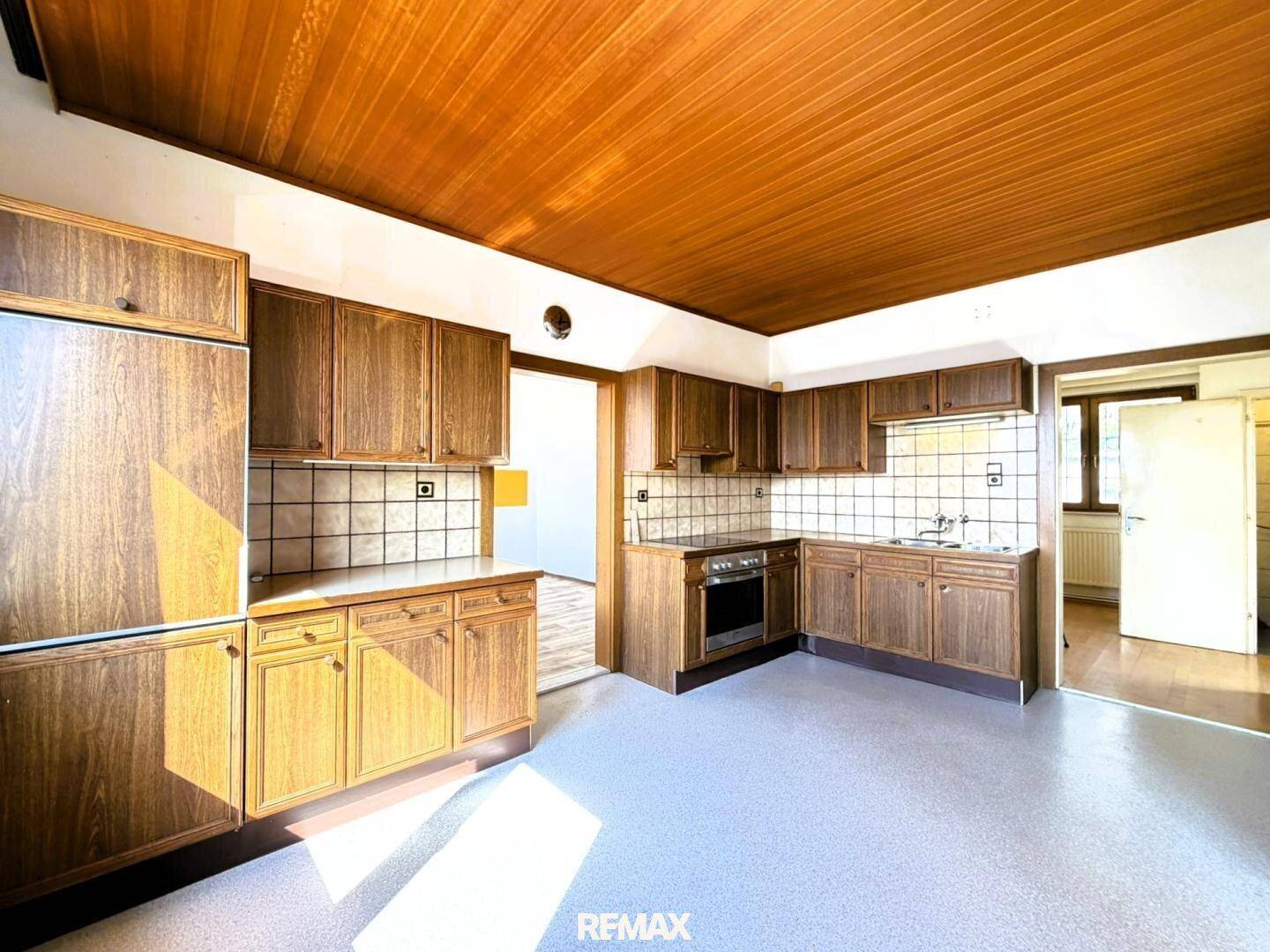 Traditionelle Küche mit Holzdecke und braunen Schränken, ausgestattet mit Herd und Spüle.