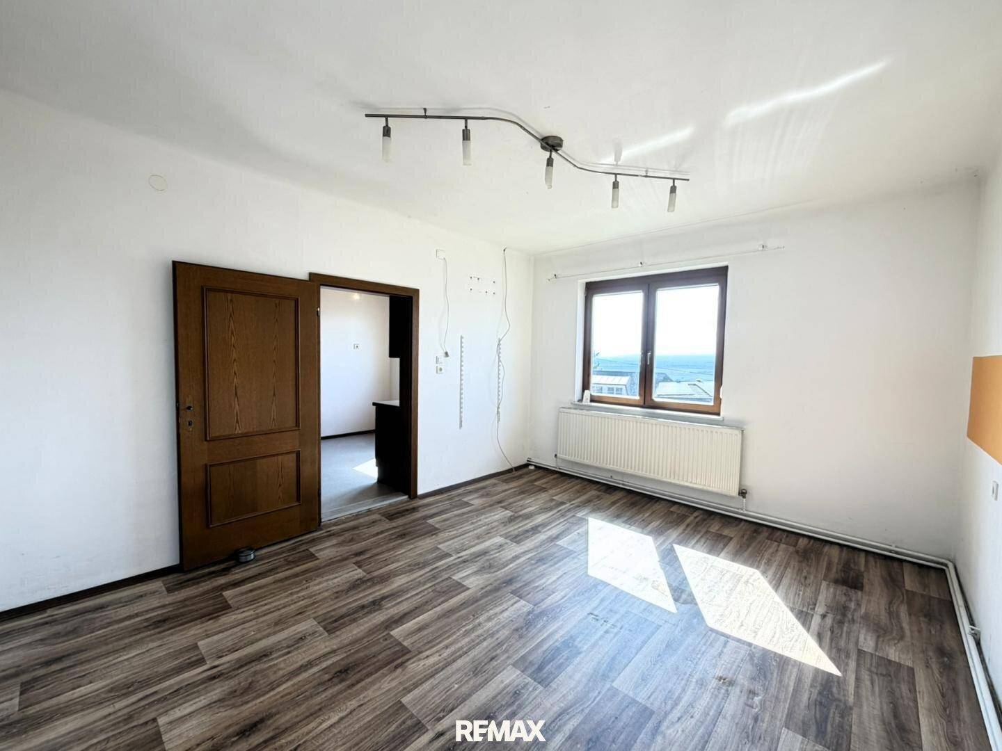 Helles Wohnzimmer mit Holzboden und großem Fenster, bietet viel Tageslicht und Ausblick.