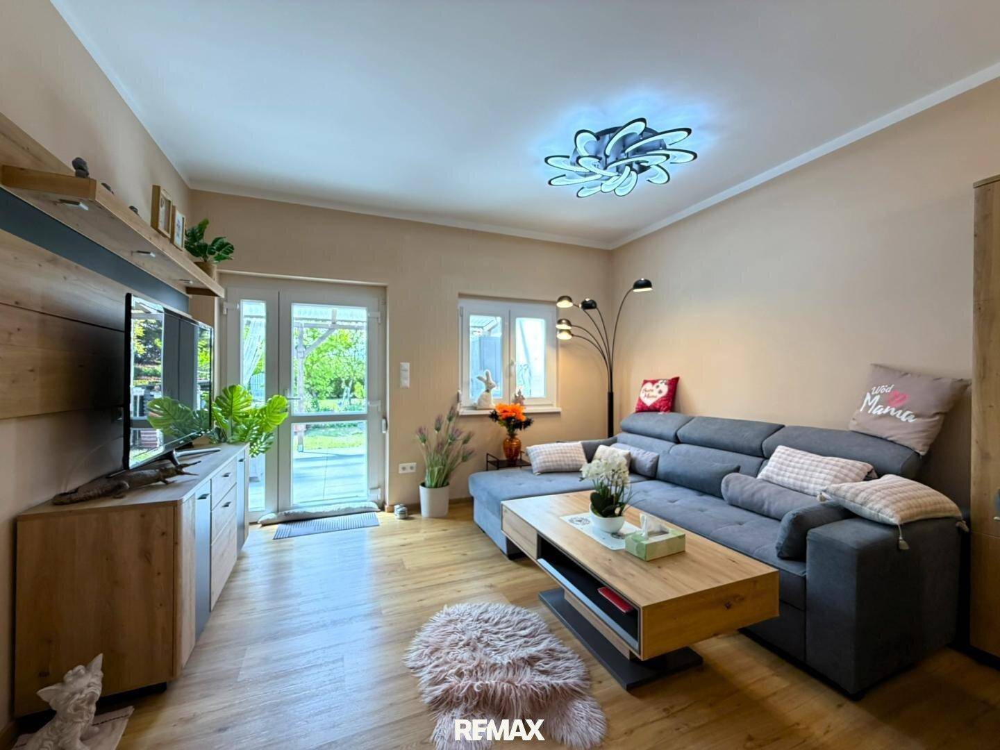 Helles Wohnzimmer mit großem Sofa, Holzboden und Zugang zum Garten.