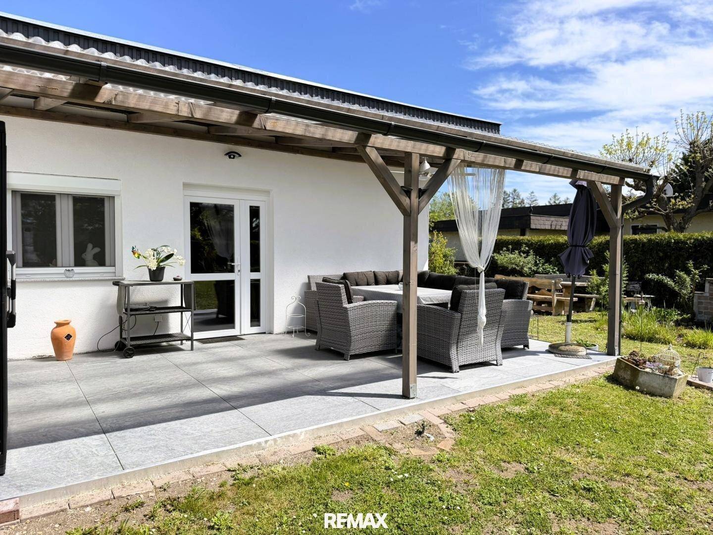 Überdachte Terrasse mit modernen Gartenmöbeln und Blick in den grünen Garten.