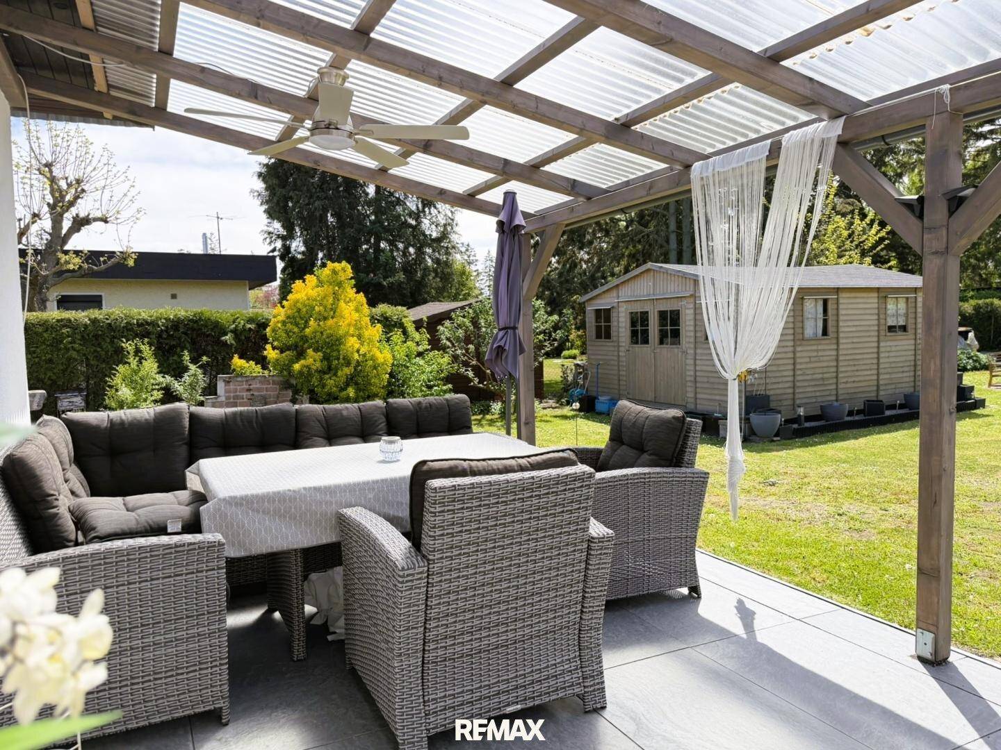 Überdachte Terrasse mit bequemen Gartenmöbeln und Blick auf den Garten und Geräteschuppen.