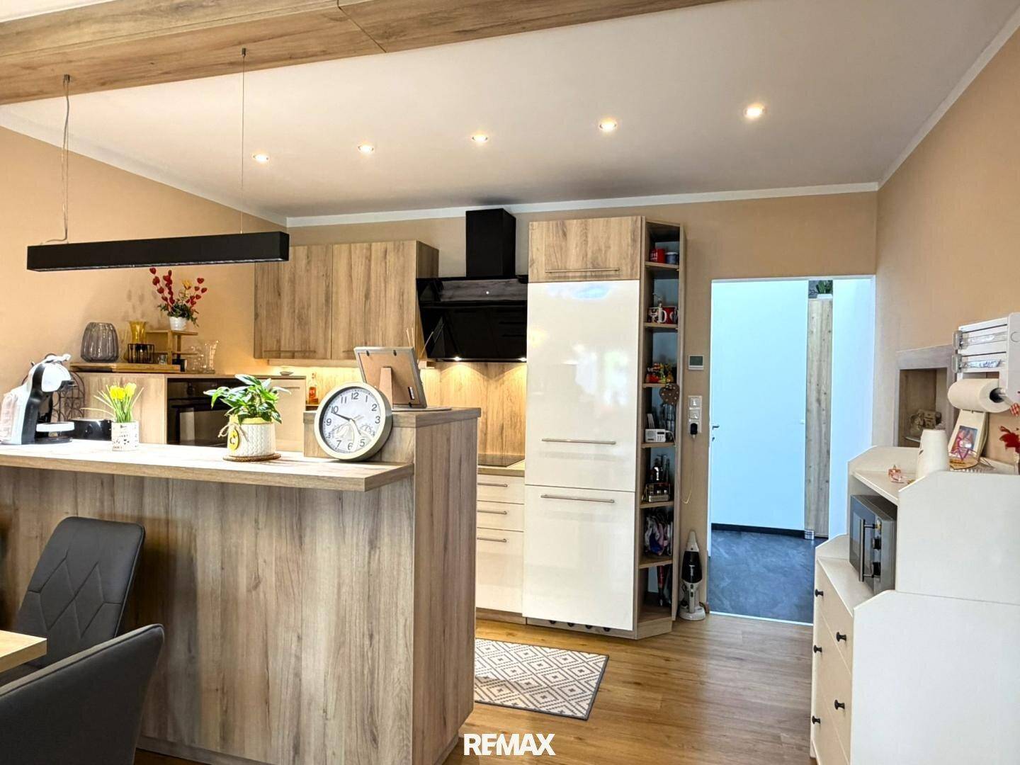 Moderne Einbauküche mit Holz- und Hochglanzfronten, Kochinsel und Essbereich.
