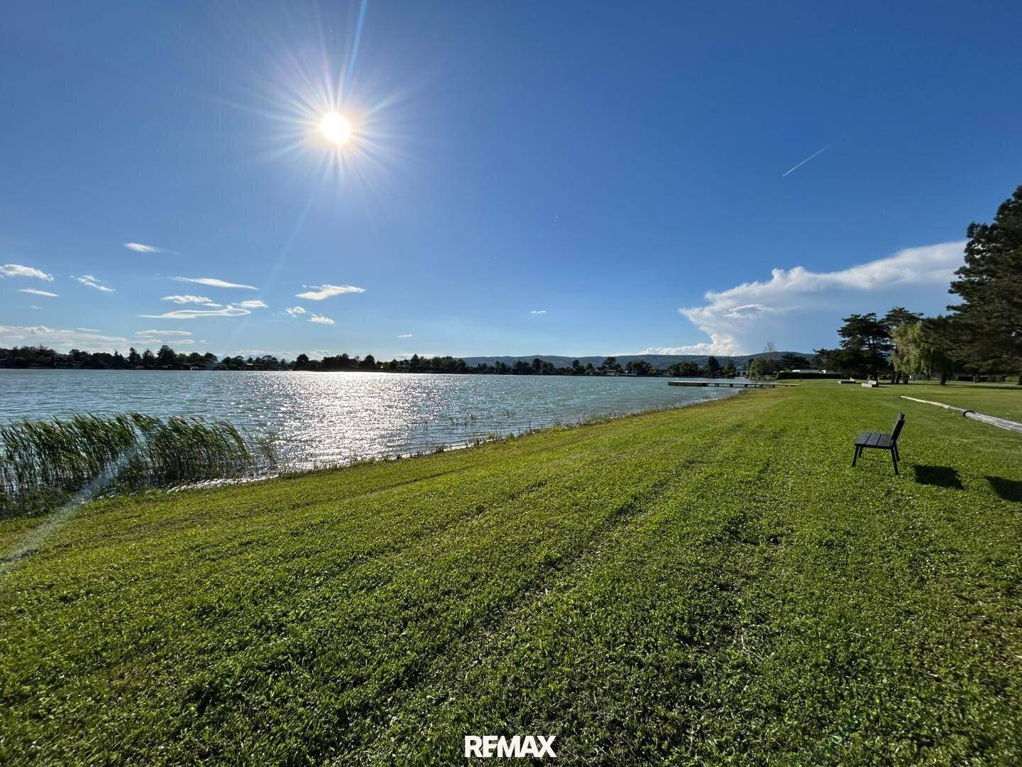 Malerischer Seeblick unter strahlend blauem Himmel mit grünen Ufern und Bäumen.