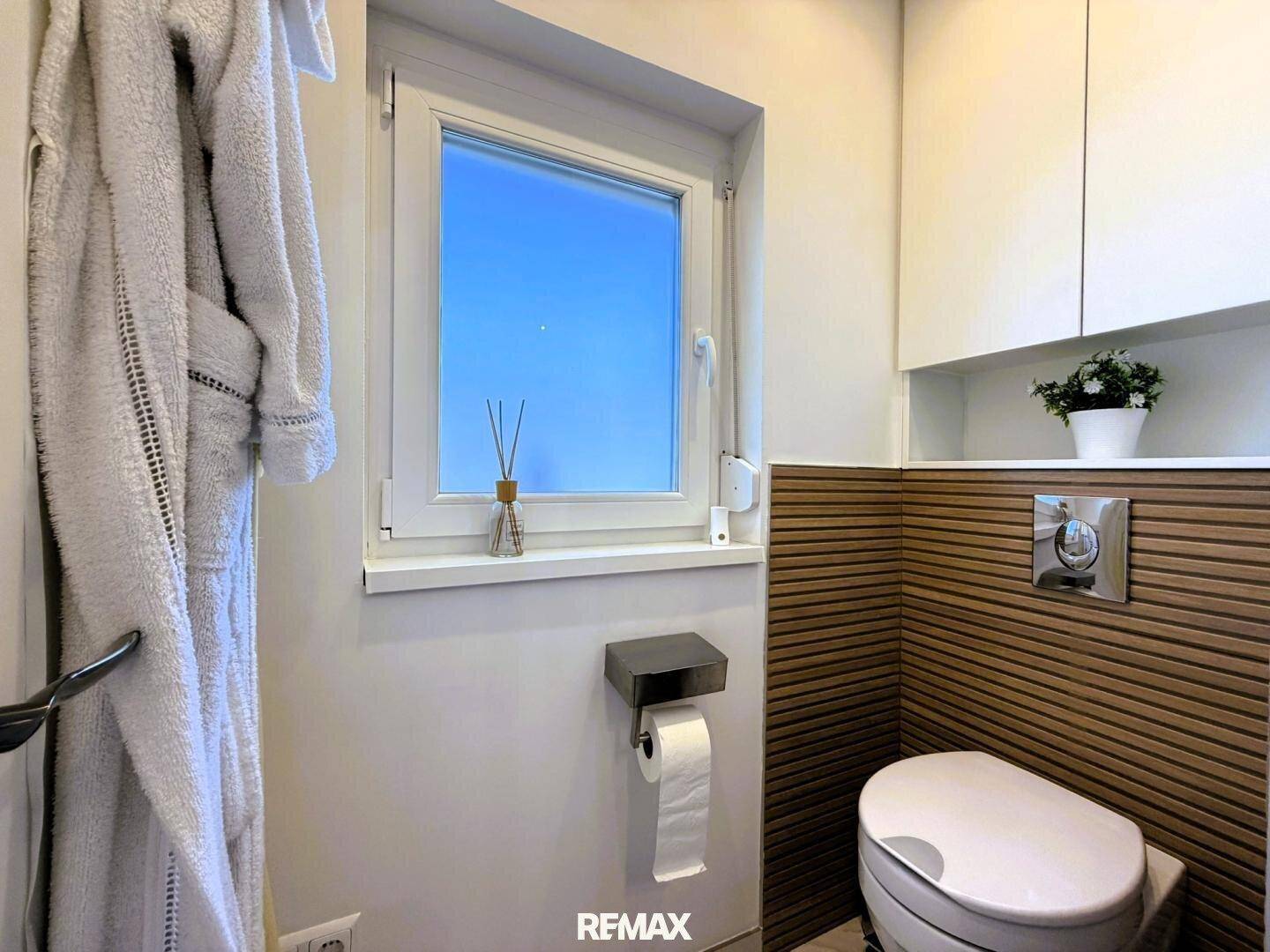 Separates WC mit Fenster, Wand-WC und Holzverkleidung für eine moderne Optik.