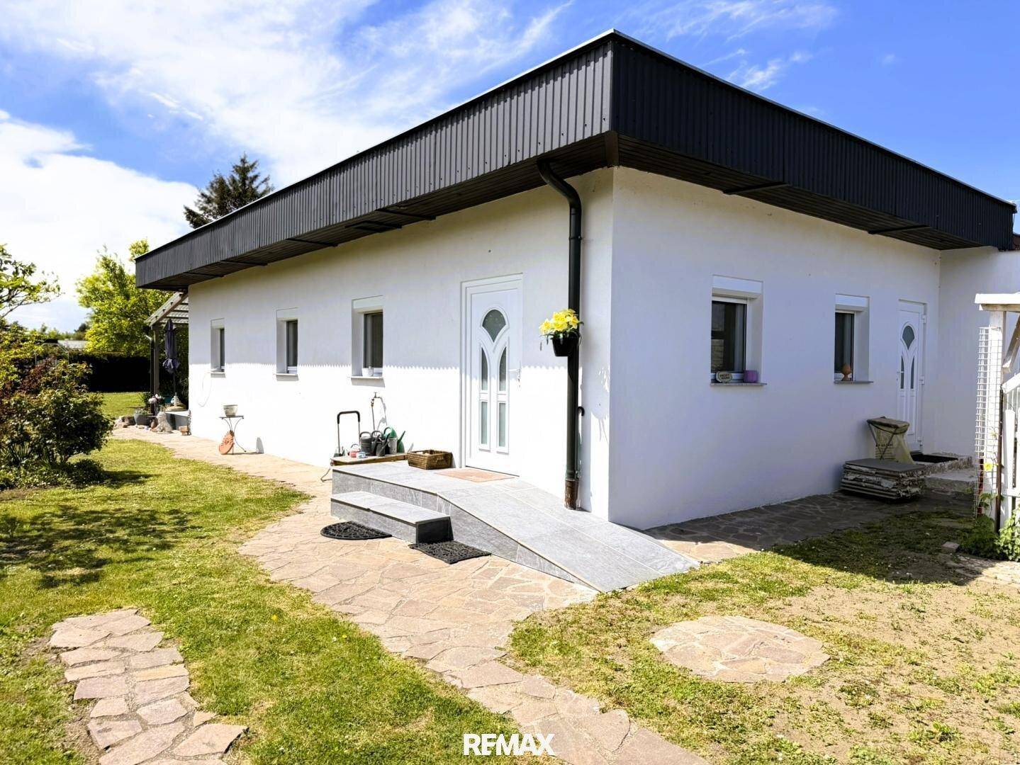 Modernes Einfamilienhaus mit weißer Fassade, dunklem Dach und gepflegtem Vorgarten.