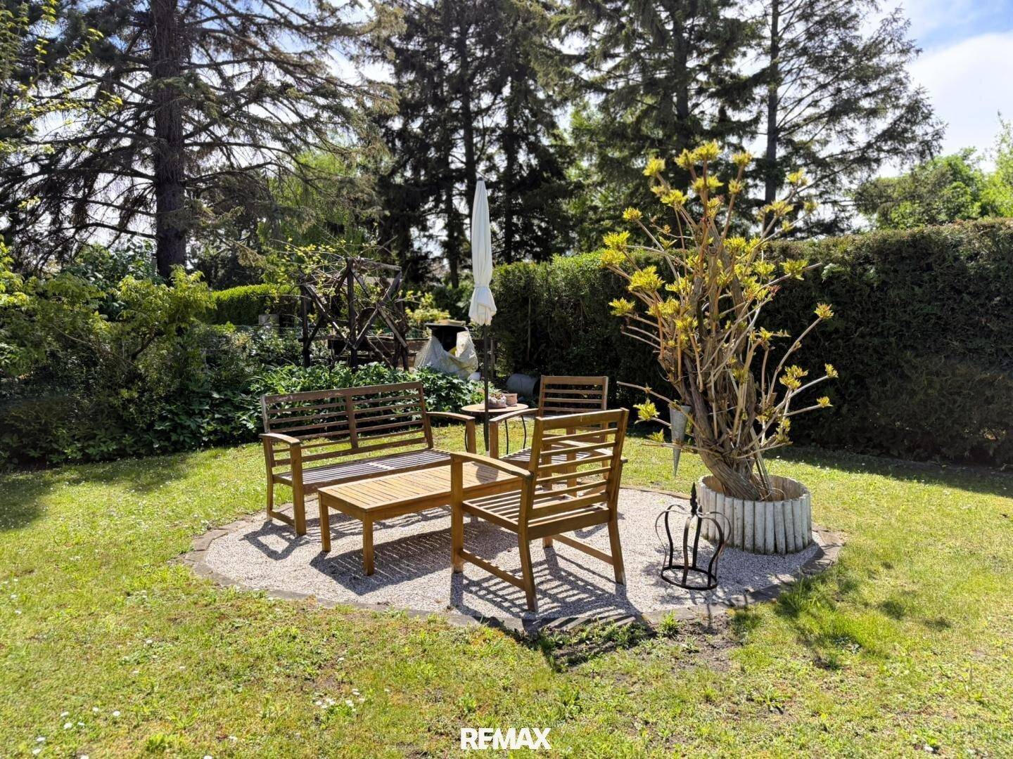 Gemütlicher Sitzbereich im Garten mit Holzmöbeln, umgeben von Hecken und Bäumen.
