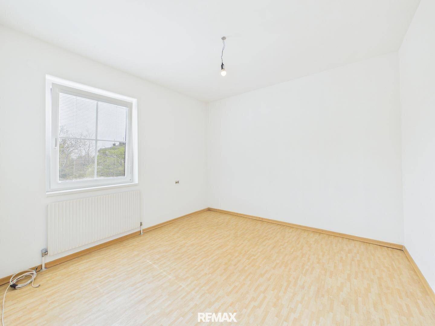 Leeres Schlafzimmer mit Laminatboden und einem großen Fenster für viel Tageslicht.