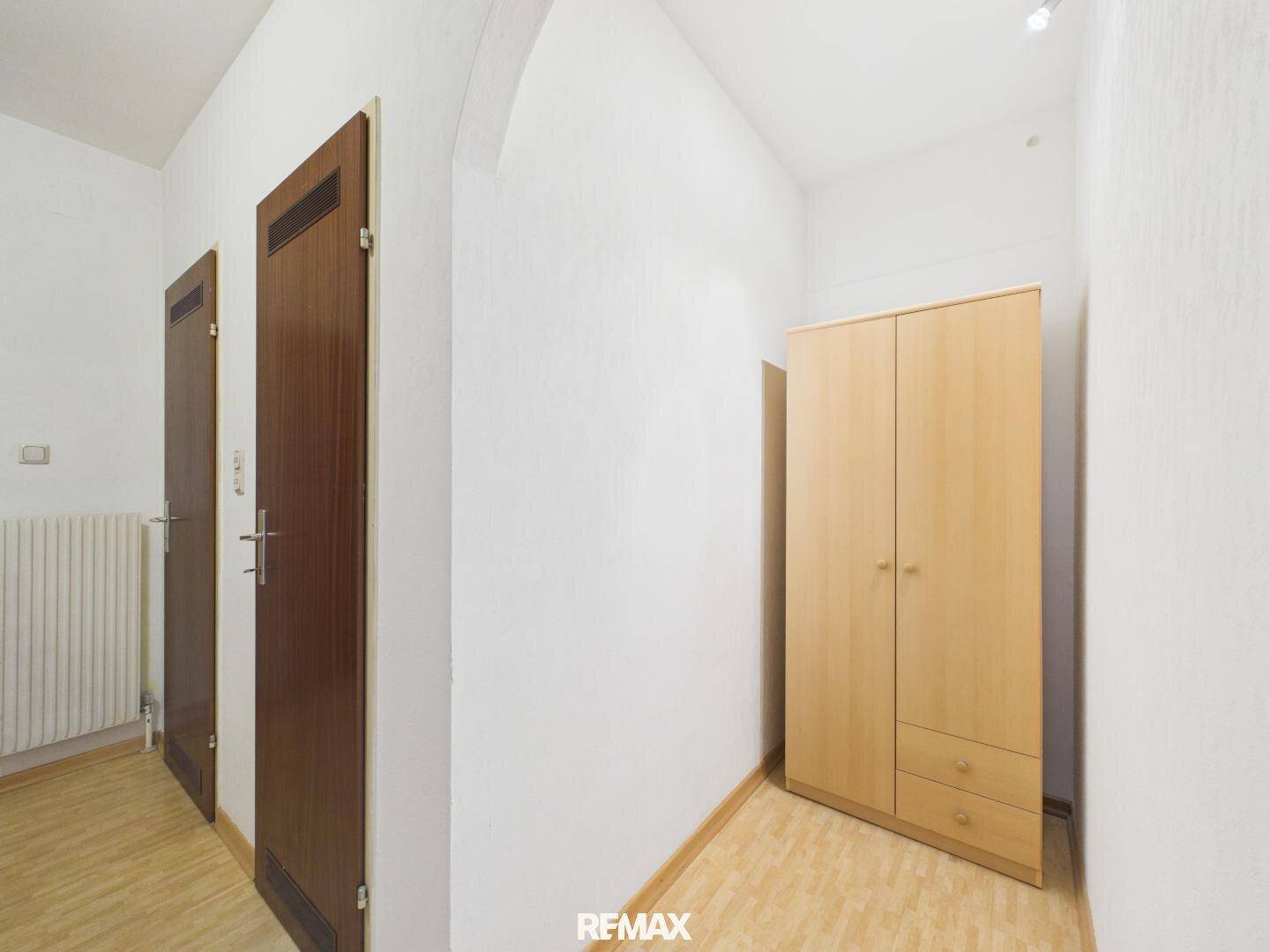 Heller Flur mit Laminatboden und einem einfachen Holzschrank, der Stauraum bietet.