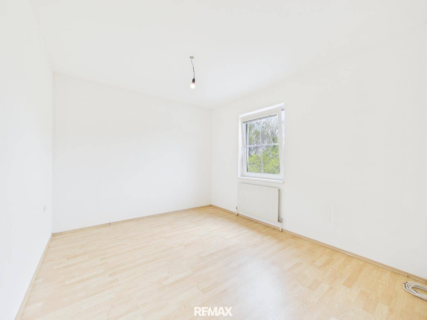 Helles Schlafzimmer mit Laminatboden und einem Fenster, das eine grüne Aussicht bietet.