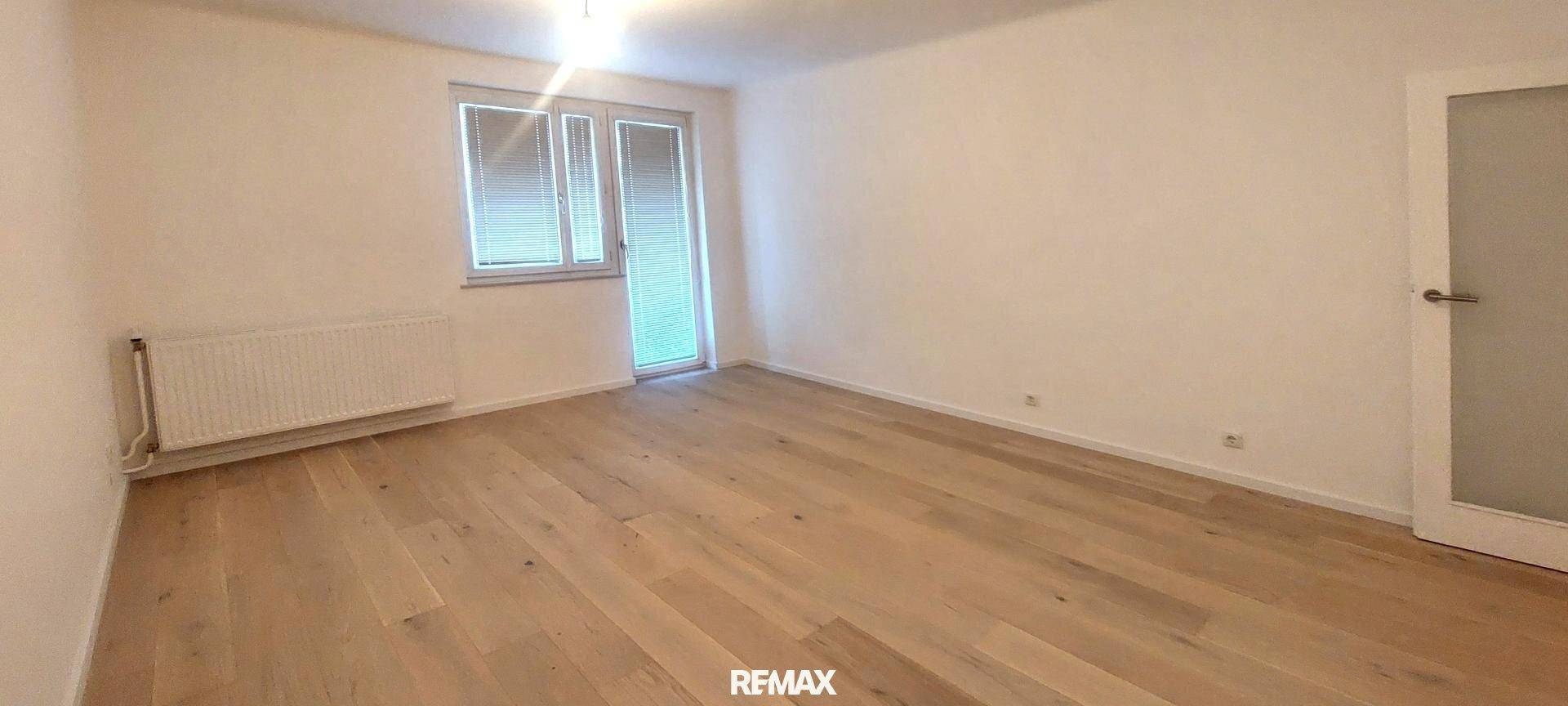 Geräumiges Zimmer mit Holzboden, weißen Wänden und Zugang zu einem Außenbereich.