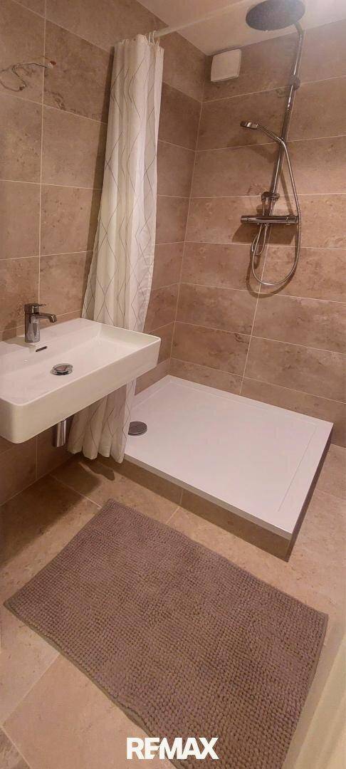Modernes Badezimmer mit beigefarbenen Fliesen, Waschbecken und ebenerdiger Dusche.