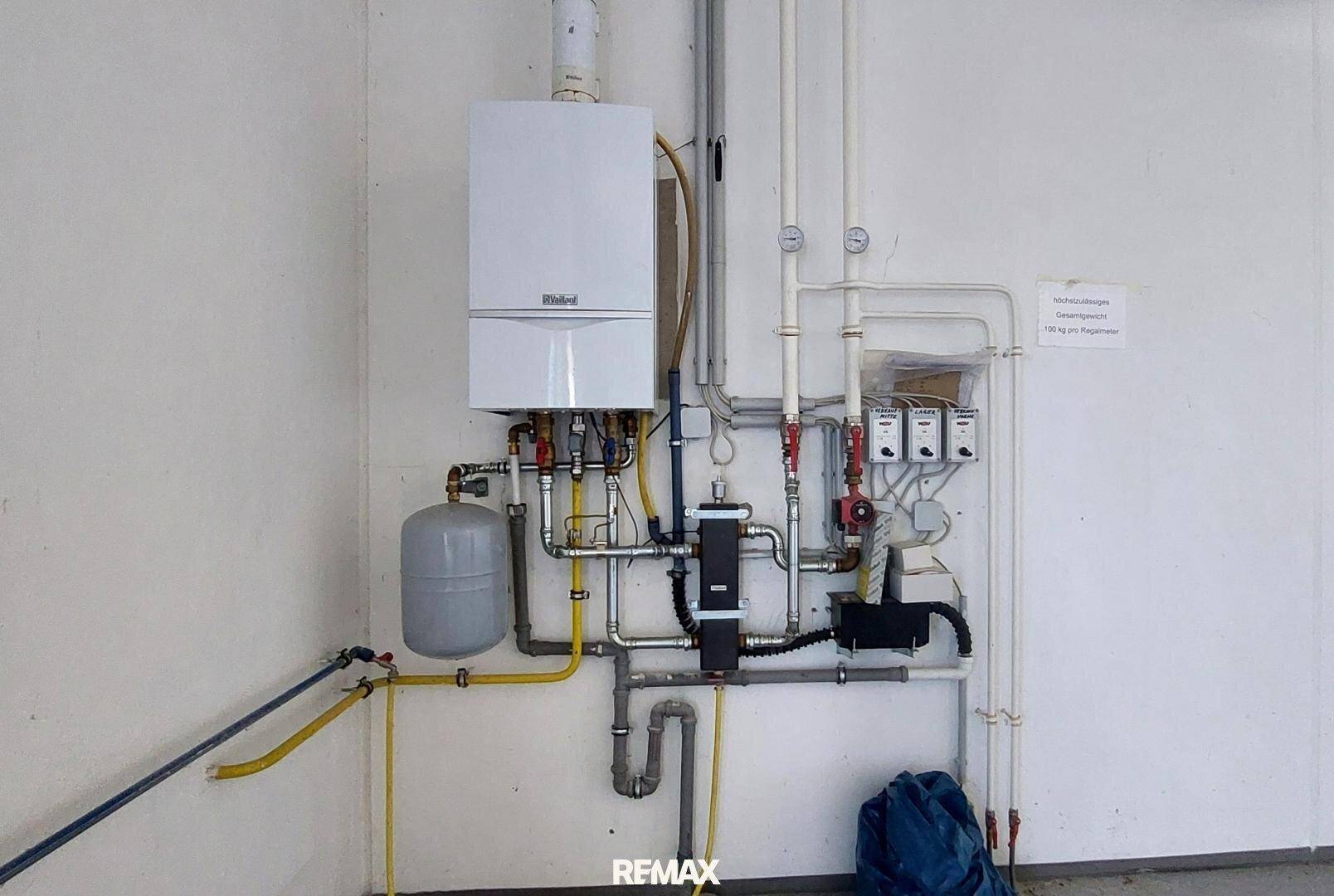 Wandmontiertes Heizsystem mit zahlreichen Rohren und Messgeräten in einem Technikraum.
