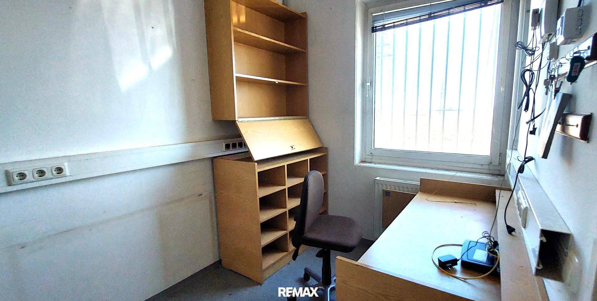 Kleines Büro mit einem Fenster, einem Holzschreibtisch und einem passenden Regal an der Wand.