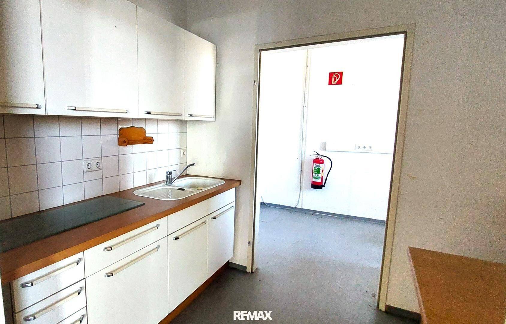 Kleine Küchenzeile mit weißen Schränken, Spüle, Kochfeld und gefliestem Spritzschutz.