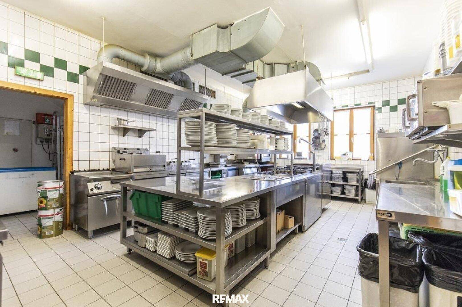 Professionelle Großküche mit Edelstahlgeräten, Ablufthauben und gefliesten Wänden, bereit zum Kochen.