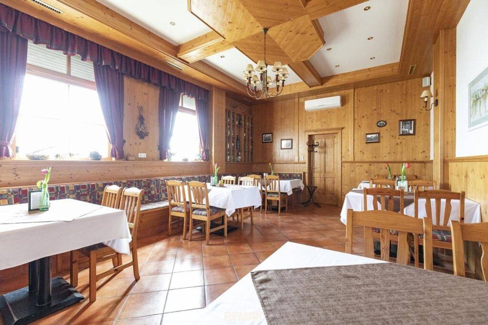 Rustikaler Speisesaal mit großen Fenstern, Holzvertäfelung und traditionellen Möbeln, sehr hell.