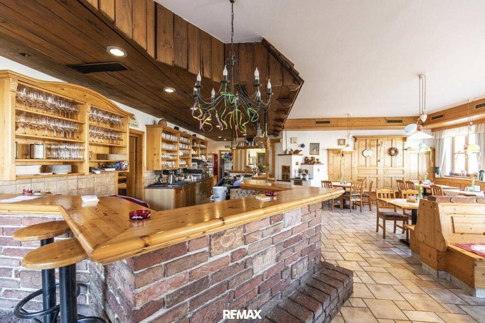 Rustikale Bar mit Holzelementen und Ziegelmauerwerk, angrenzend an einen traditionellen Gastraum.