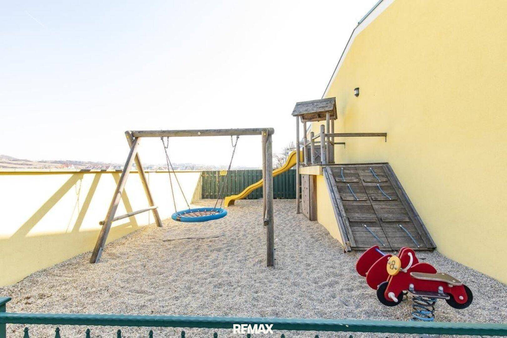 Detailansicht eines Kinderspielplatzes mit Schaukel, Rutsche und Klettergerüst auf Sandboden.