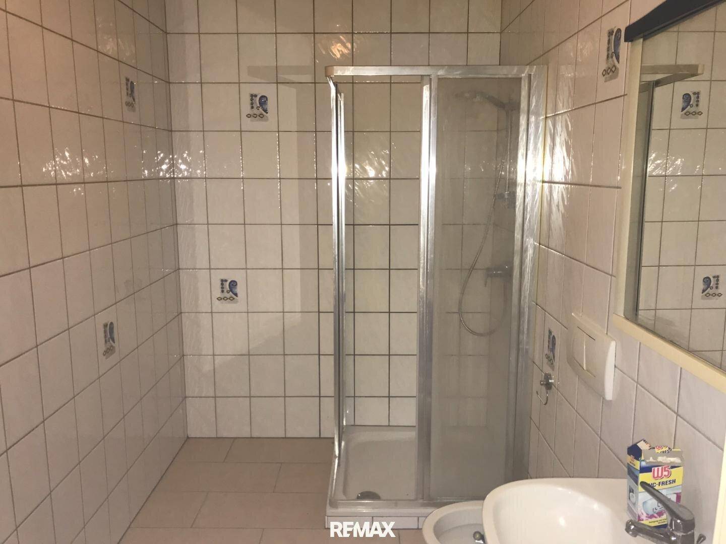 Badezimmer mit Duschkabine, Waschbecken und WC, komplett gefliest in Weiß, sauber und hell.