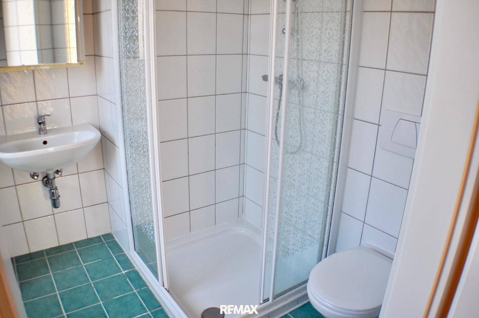 Badezimmer mit Duschkabine, Waschbecken und WC, gefliest in Weiß und Grün, funktional und hell.