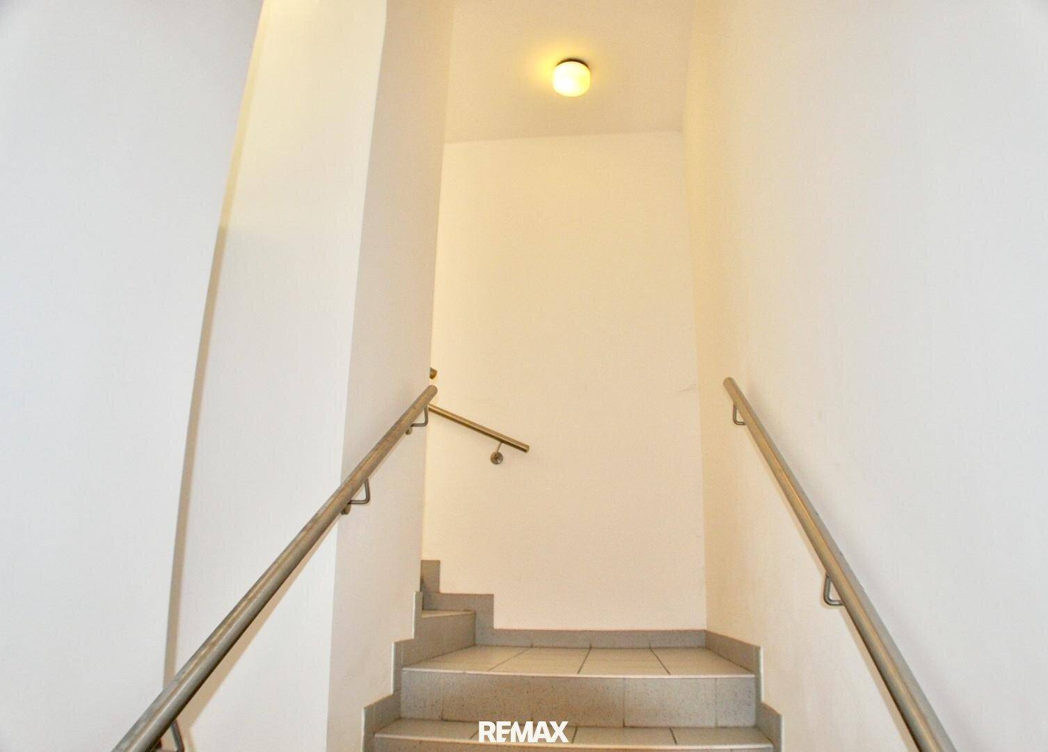 Heller Treppenaufgang mit Fliesenboden und Edelstahlgeländer in einem Mehrfamilienhaus, gut beleuchtet.